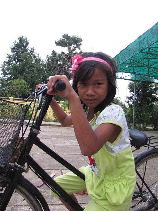 Young girl in green overalls with pink headband on bicycle