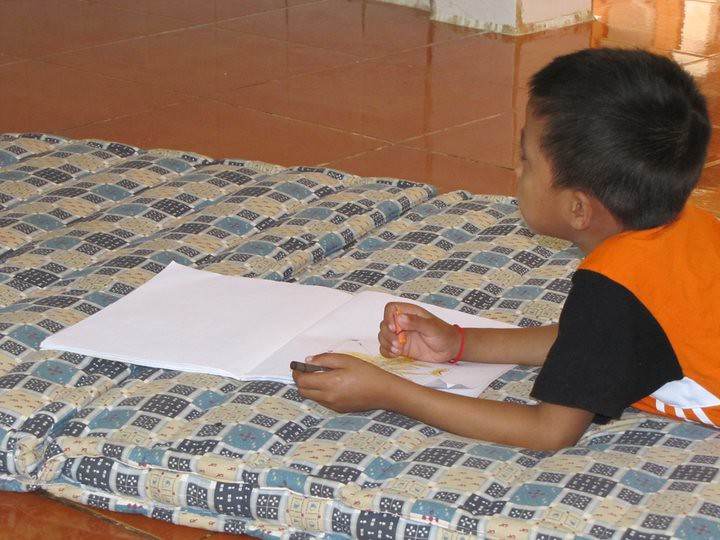 Boy drawing on paper while lying on patterned mat