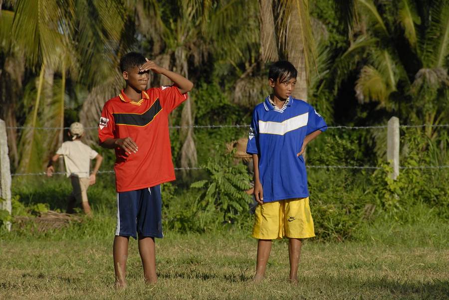 Two boys standing on grass field in red and blue soccer jerseys