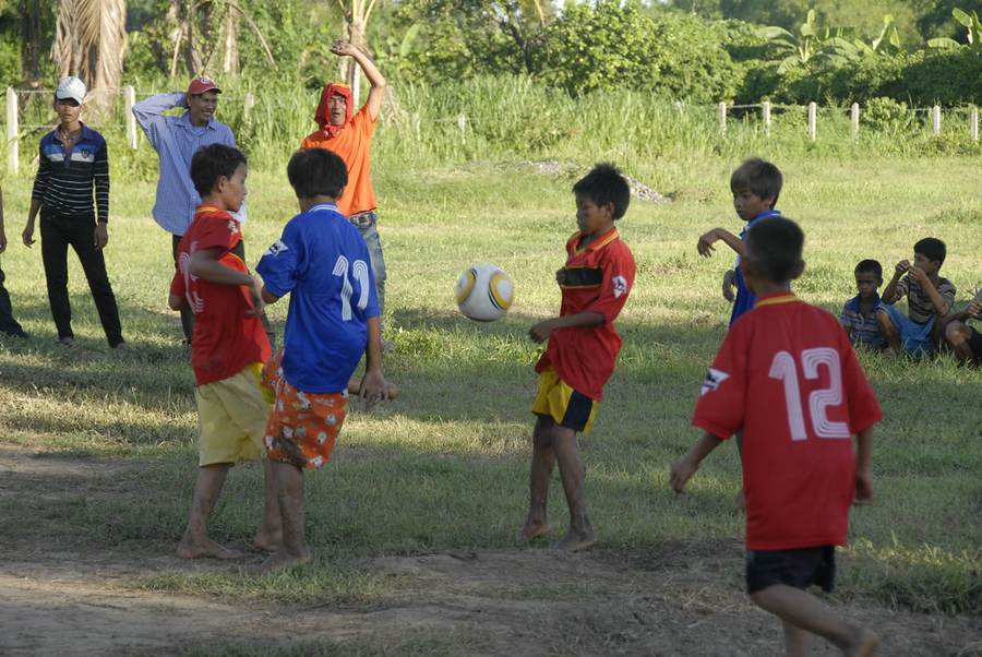 Children playing soccer with adults watching