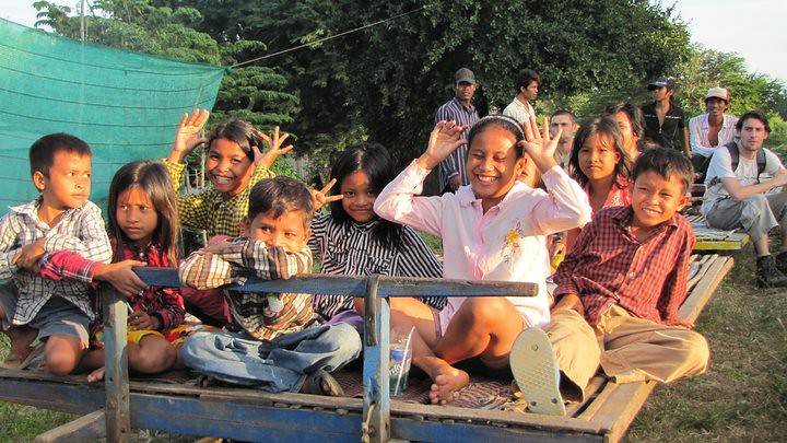 Group of children and volunteers sitting on blue trailer waving