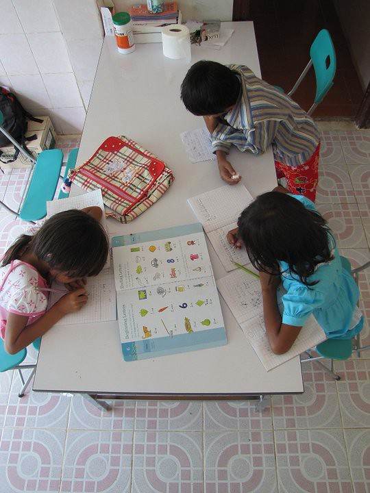 Three children studying at table with notebooks and textbook